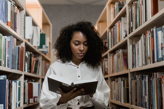 African American woman with curly hair standing in a library reading a book.
